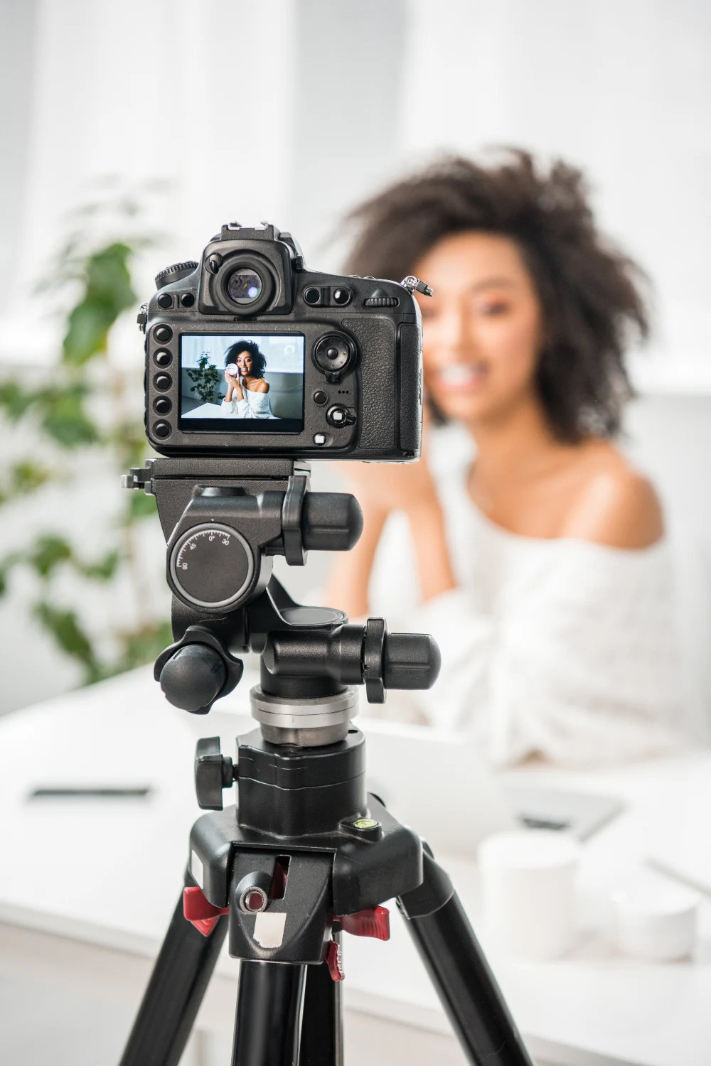 Digitalkamera på stativ som filmar mörk kvinna i vitt